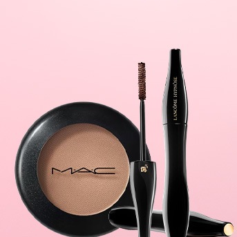Puder MAC w czarnej puderniczce obok brązowego tuszu do rzęs Lancôme Hypnôse z aplikatorem na różowym tle.