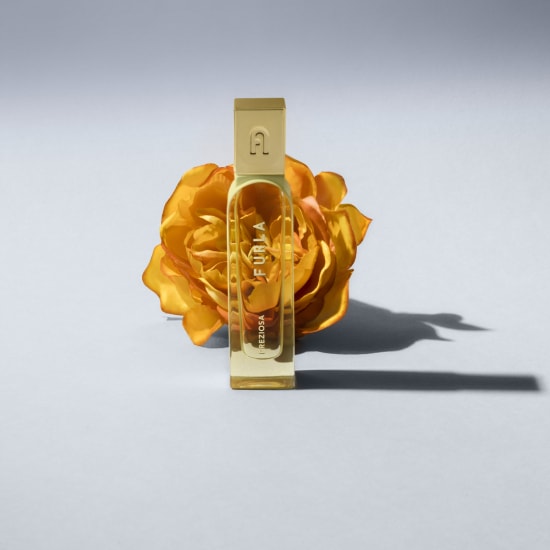 Butelka perfum Furla Preziosa o pojemności 100 ml stoi na tle pomarańczowej róży, emanując elegancją i ciepłem.