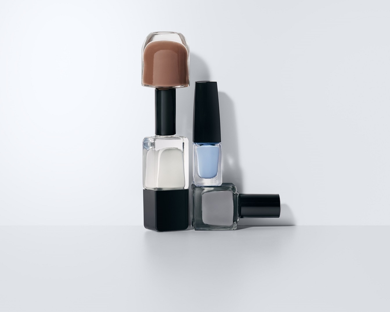 Verschiedene Nagellackfarben sind in durchsichtigen Glasflaschen mit schwarzen Deckeln gestapelt, darunter Braun-, Weiß-, Blau- und Grautöne.