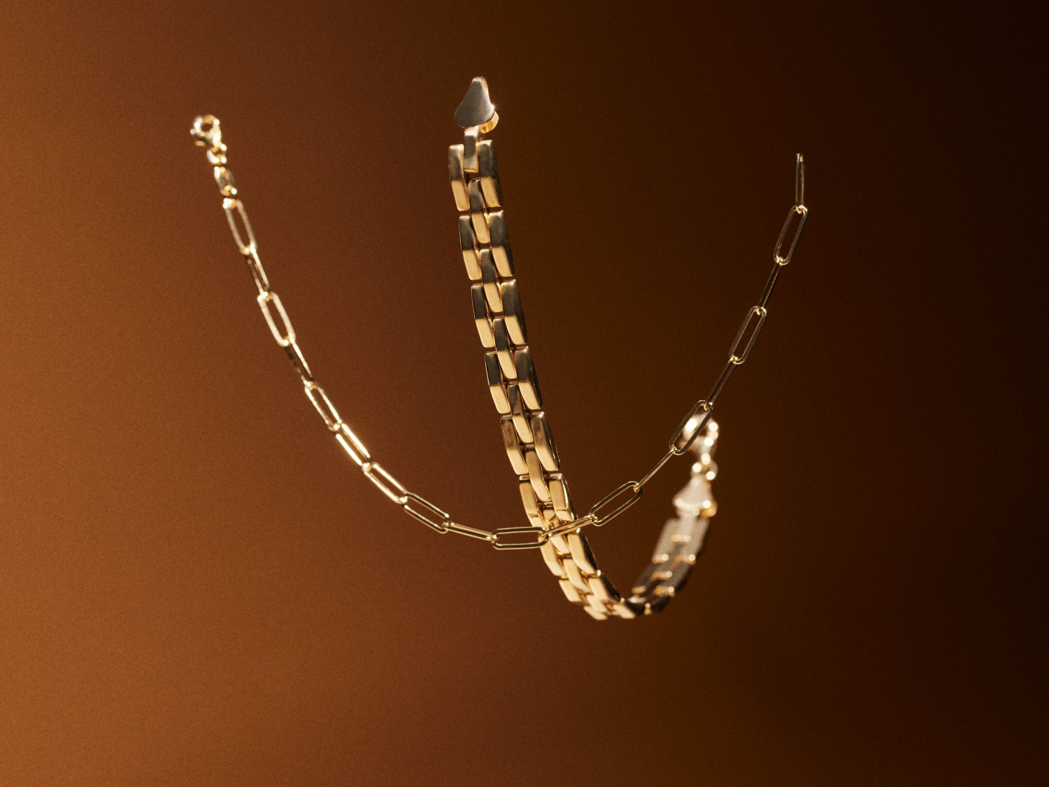 Gouden ketting met verschillende schakeldesigns zweeft tegen een bruine achtergrond, een elegante toevoeging aan elke outfit.