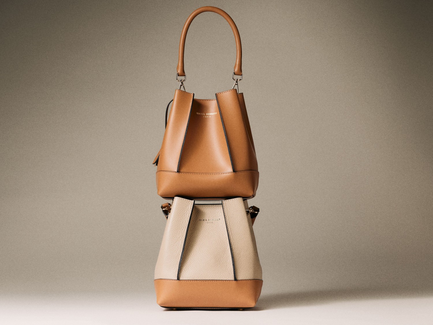 Twee Isabel Bernard handtassen, de bovenste is bruin leer met een handvat, de onderste is beige met bruine accenten.