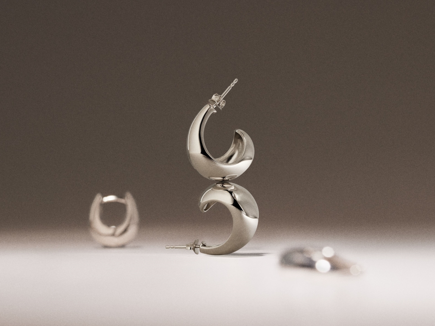 Gepolijste zilverkleurige oorringen in een halvemaanvorm, elegant gestapeld op een zachte, neutrale achtergrond.