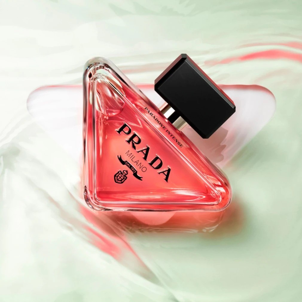 De Prada Paradoxe Intense Eau de Parfum, gehuld in een driehoekige flacon met een zwarte dop, straalt een intense, roze gloed uit.