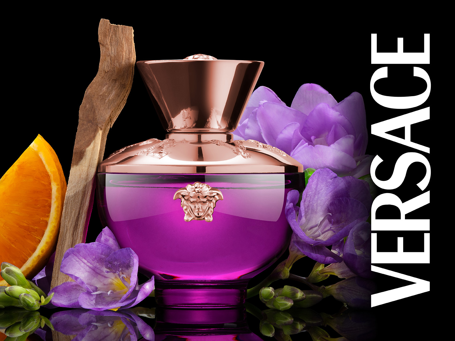 Butelka fioletowych perfum Versace otoczona jest kwiatami, pomarańczą i kawałkiem drewna na czarnym tle.