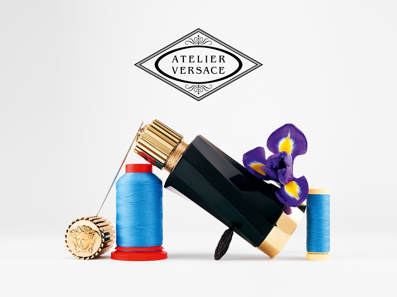 Czarny flakon Atelier Versace z niebieską nicią, igłą i fioletowym kwiatem irysa tworzą elegancką kompozycję.