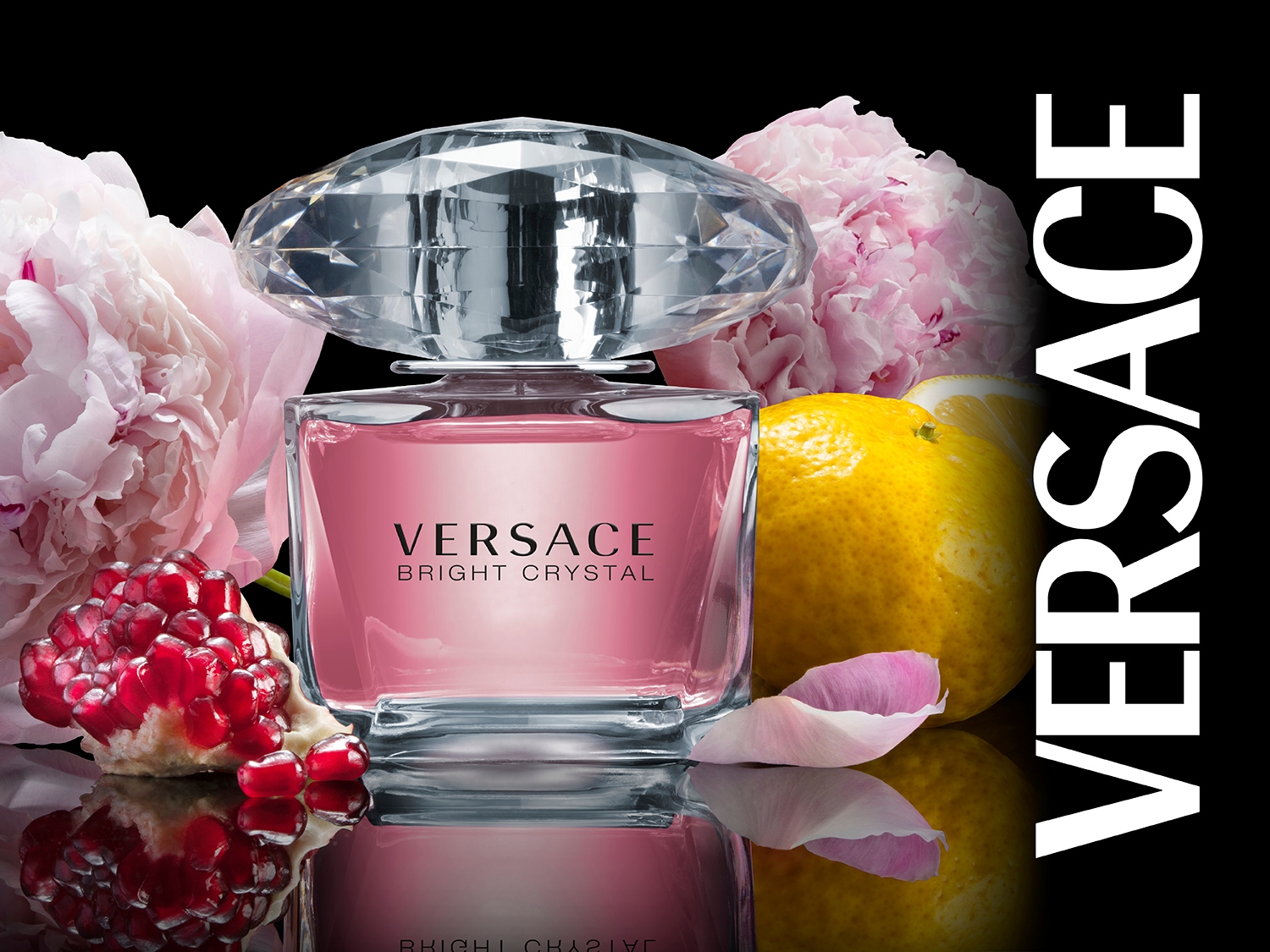 Butelka Versace Bright Crystal z różową zawartością i kryształową nakrętką, otoczona kwiatami piwonii, granatem i cytryną na czarnym tle.