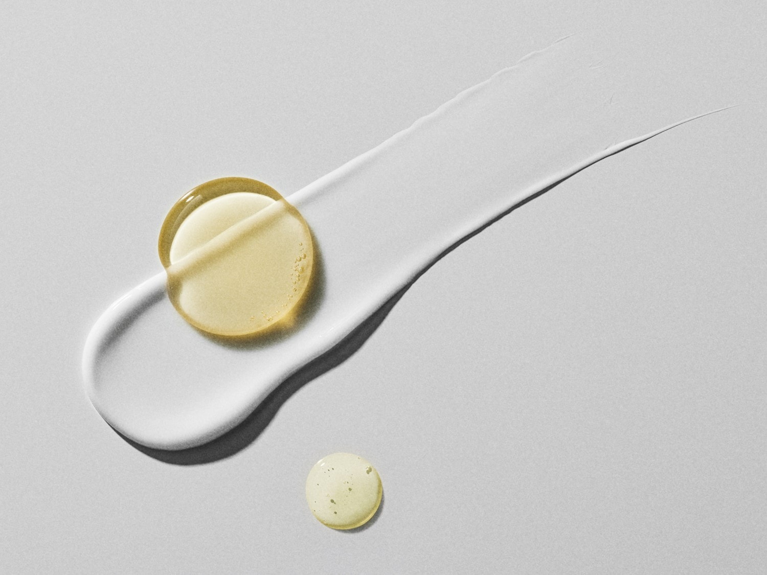 Nahaufnahme eines weißen Cremestrichs mit einem gelben Öl-Gel-Pad darauf und einem weiteren kleinen Tropfen daneben, der die Textur und Konsistenz des Produkts hervorhebt.