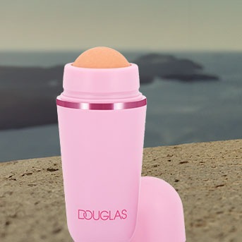 Różowy roller do twarzy Douglas z pomarańczową kulką na górze, stojący na tle morza, idealny do pielęgnacji skóry.