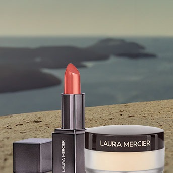 Szminka Laura Mercier w koralowym odcieniu obok słoiczka z pudrem na tle morza.