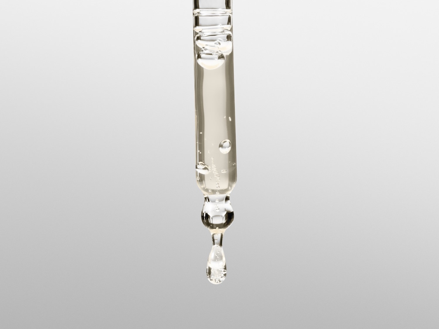 Ein durchsichtiger Glaspipette mit Serum, das einen einzelnen Tropfen freisetzt, ideal für die gezielte Anwendung von Hautpflegeprodukten.