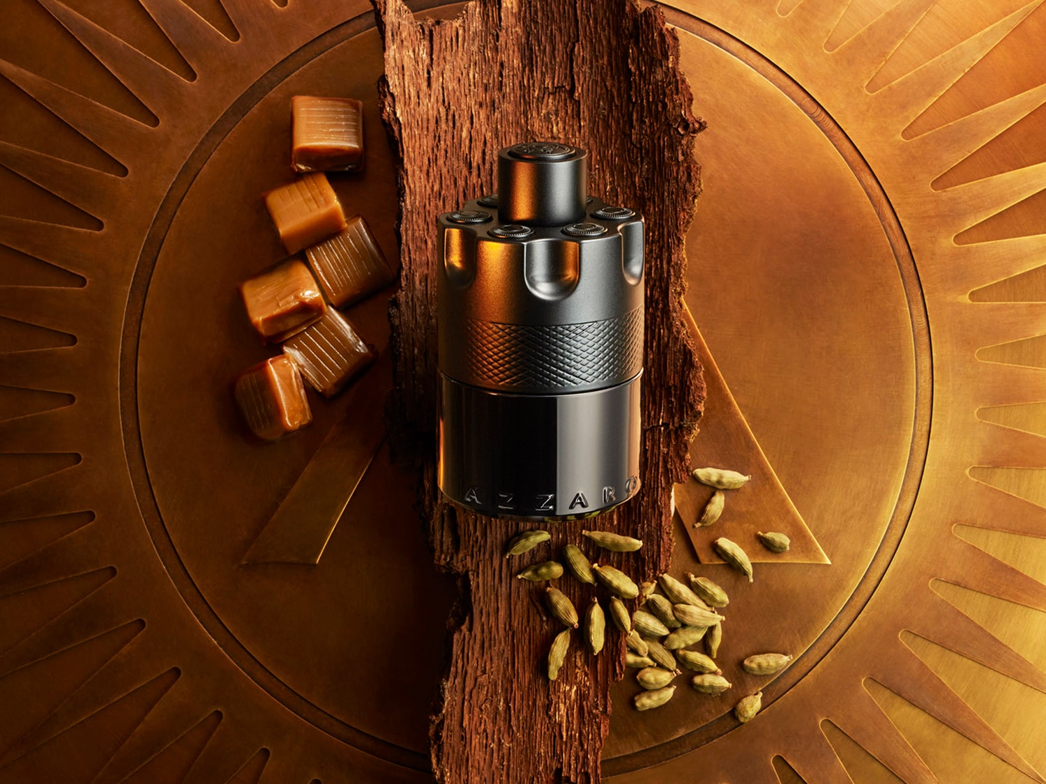 En el centro, un frasco negro de perfume Azzaro se alza sobre una base dorada adornada con dulces de caramelo y semillas de cardamomo.