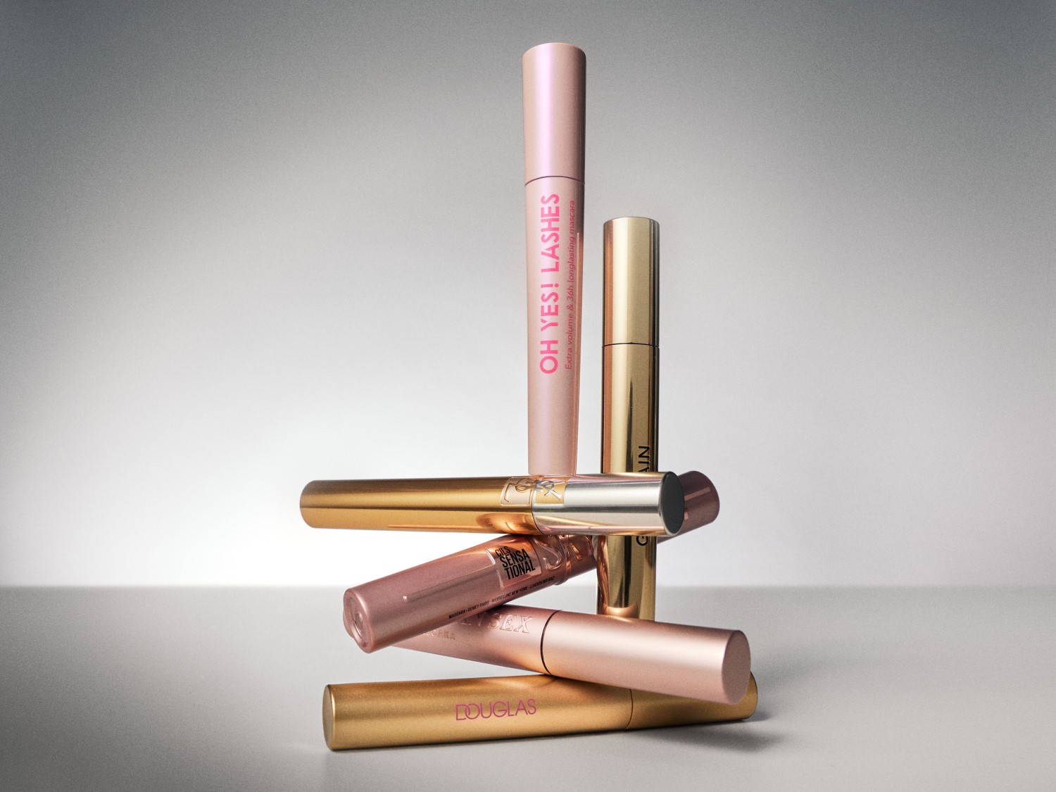 Na zdjęciu piramida z maskar do rzęs w odcieniach złota i różu, w tym Douglas i Yves Saint Laurent, oferujących efekt objętości i długotrwałości.