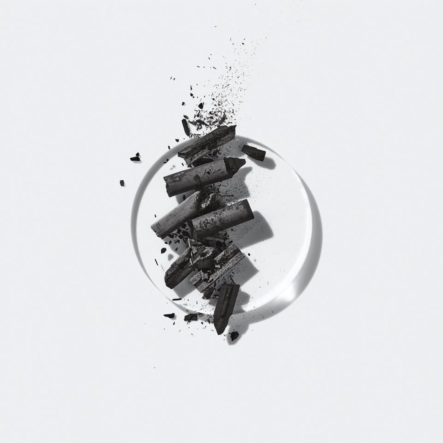 Nahaufnahme von zerbrochenen Holzkohle-Briketts auf einer durchsichtigen runden Oberfläche, die auf einem hellen Hintergrund liegen.