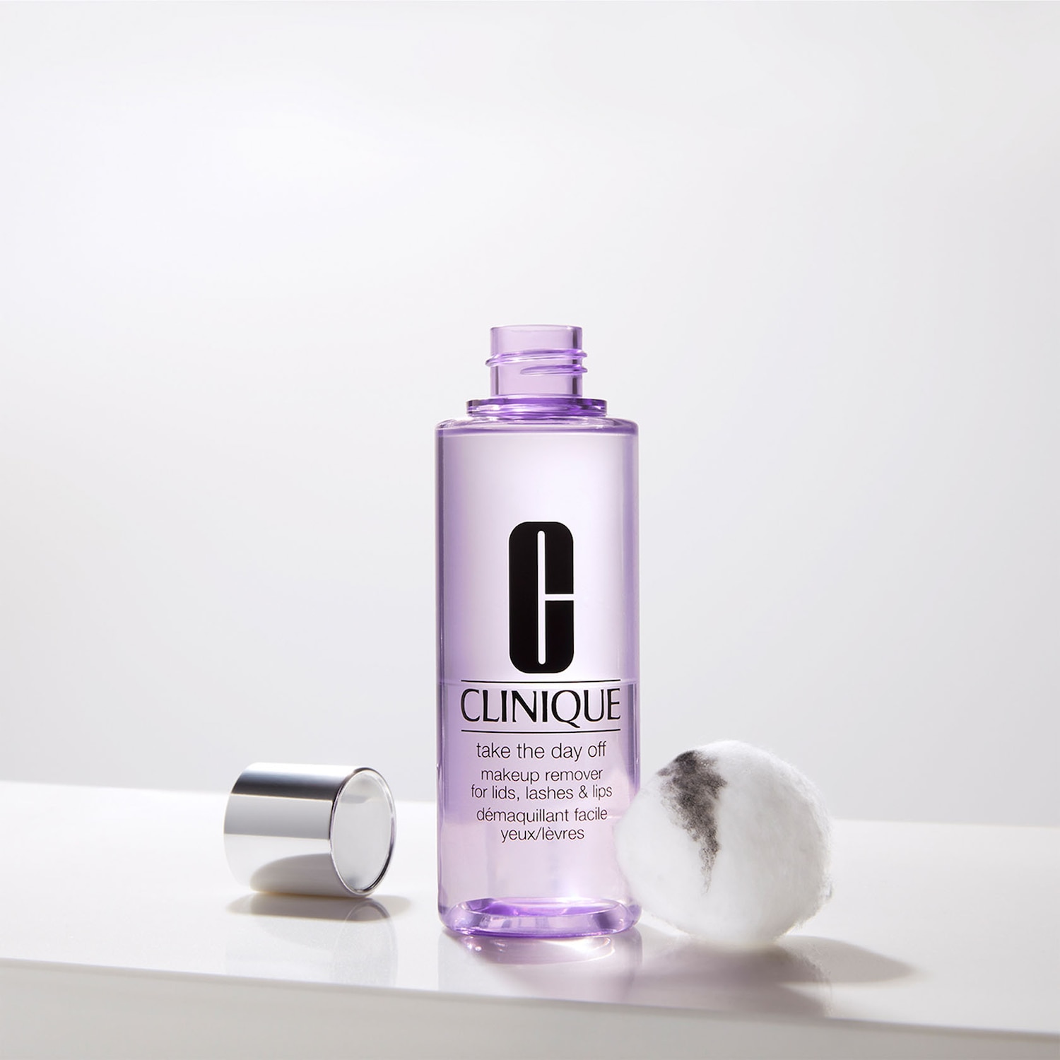 Die lila Flasche von Clinique 'Take the day off' Make-up Entferner für Augenlider, Wimpern und Lippen steht neben einem Wattepad mit Make-up Resten.