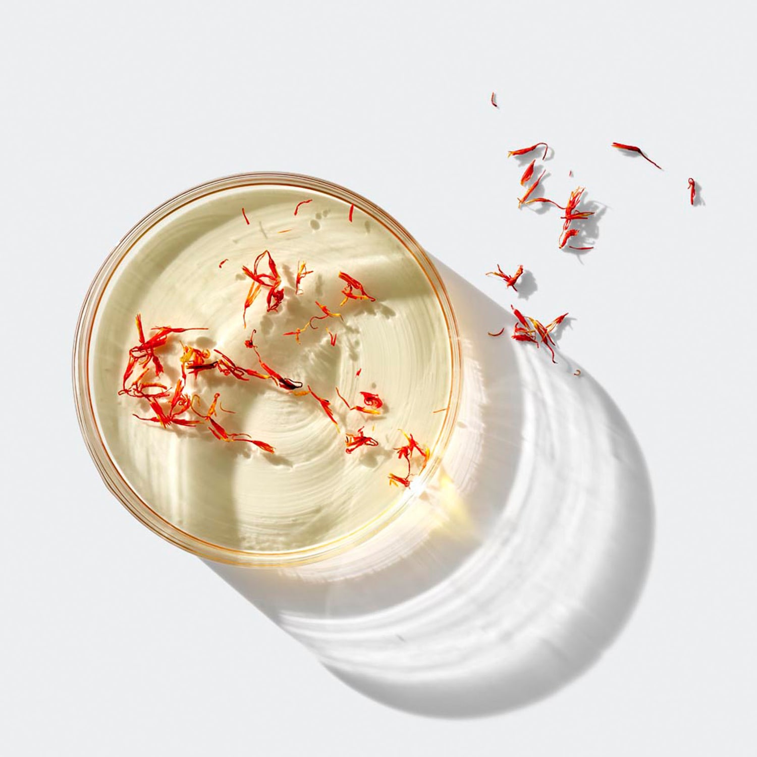 Draufsicht auf eine transparente Schale mit einer hellgelben Flüssigkeit, verziert mit roten Safranfäden, die einen Hauch von Luxus und Exotik verleihen.