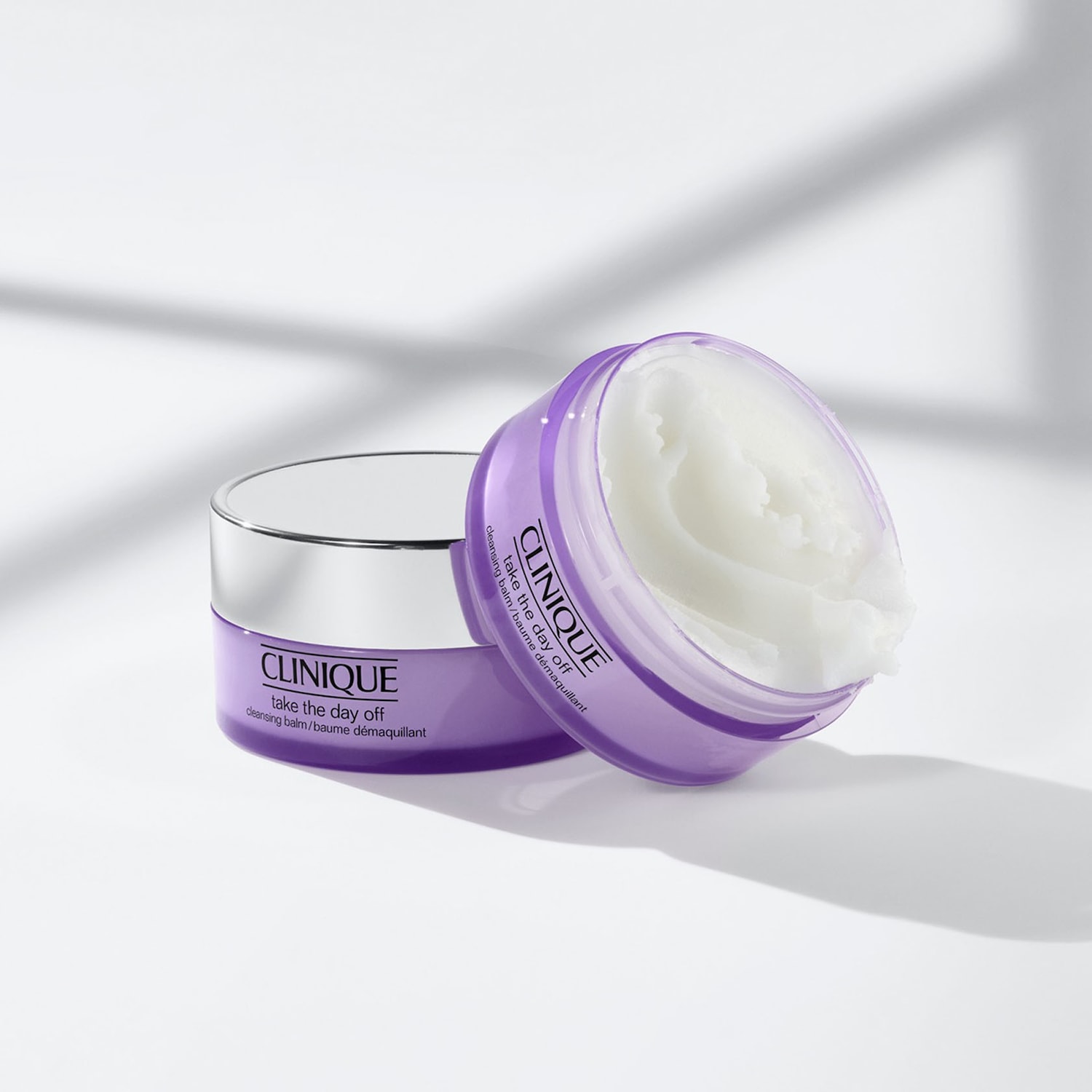 Nahaufnahme von zwei Tiegeln Clinique 'Take the Day Off' Reinigungsbalsam, einer geschlossen und der andere offen, der eine feste, weiße Creme enthüllt, alles vor einem hellen Hintergrund.