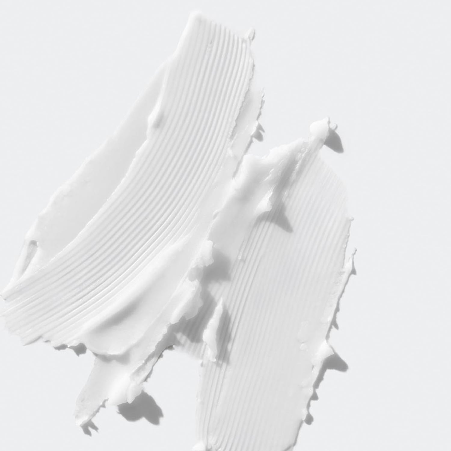 Nahaufnahme von zwei weißen, cremigen Produktabstrichen mit einer geriffelten Textur auf einem hellen Hintergrund.