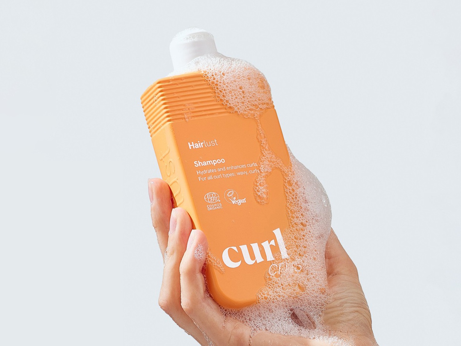 Voici un flacon orange de shampooing Hairlust Curl, conçu pour hydrater et sublimer les boucles de tous types, avec une mousse onctueuse.