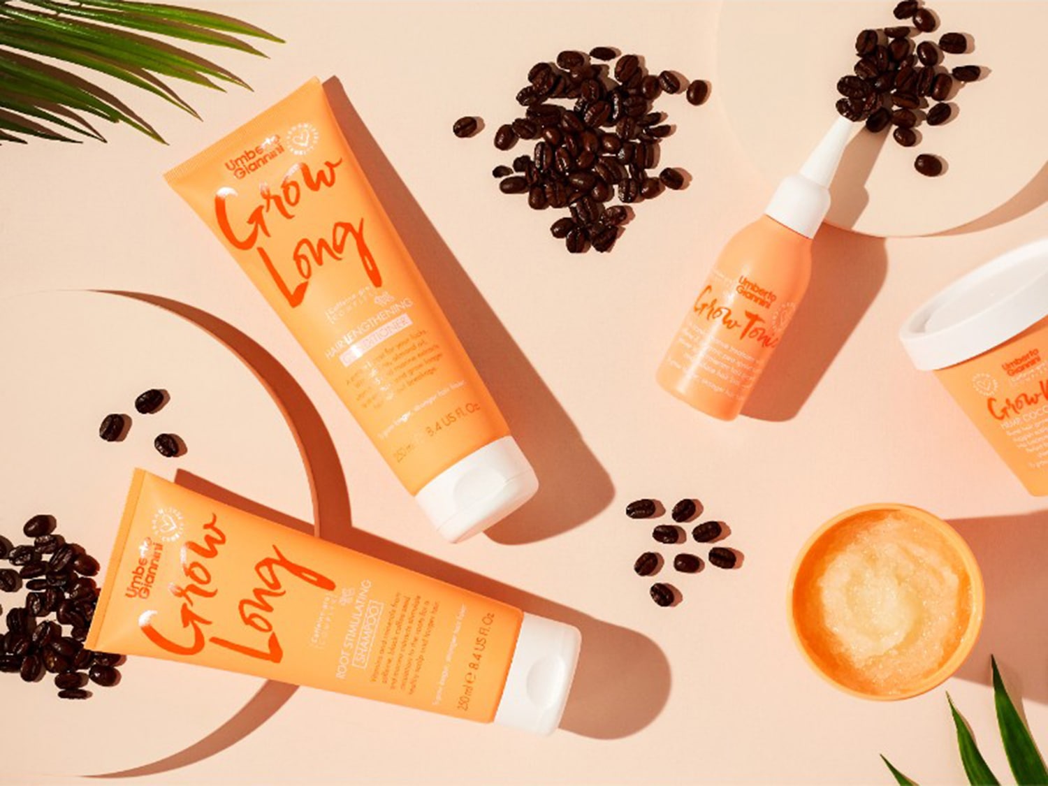 Présentation de la gamme Umberto Giannini Grow Long, comprenant un shampooing stimulant pour les racines, un revitalisant pour allonger les cheveux, un tonique et un soin du cuir chevelu, présentés avec des grains de café.