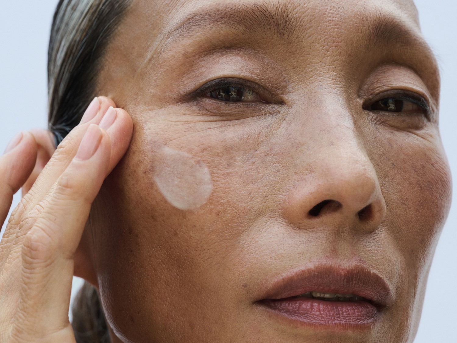 Zbliżenie na kobietę, która nakłada jasny krem na policzek, aby nawilżyć swoją skórę.