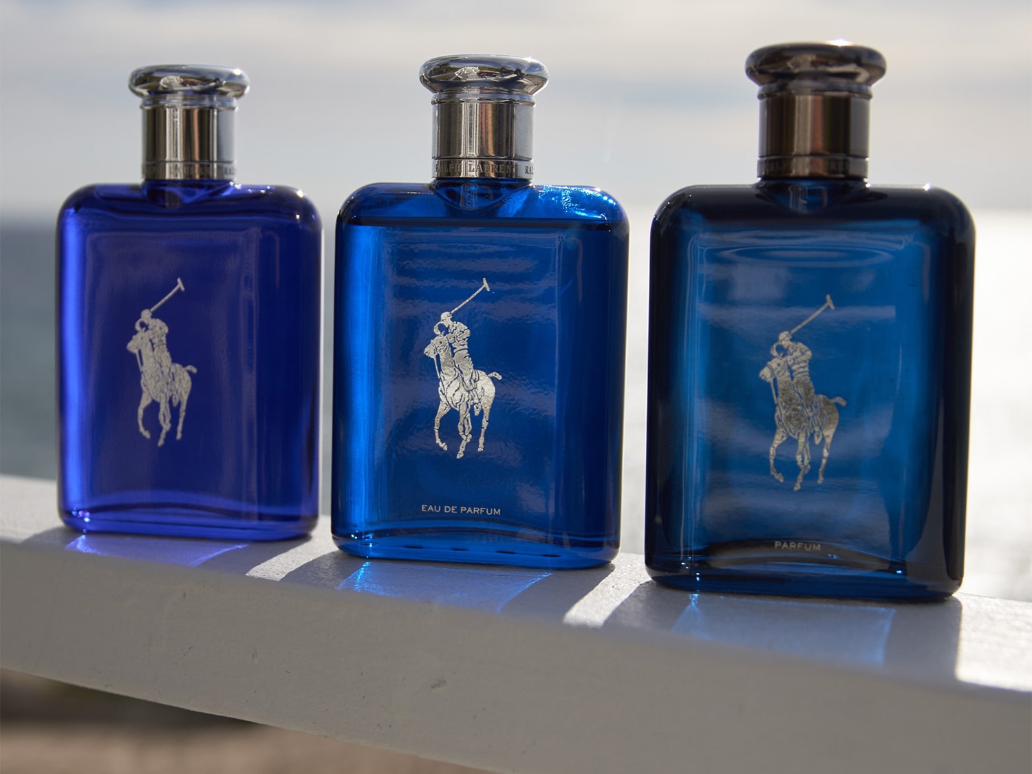 Tres frascos de perfume Ralph Lauren en tonos azules, cada uno adornado con el icónico logo del jugador de polo, ofreciendo una fragancia distintiva para cada estilo.