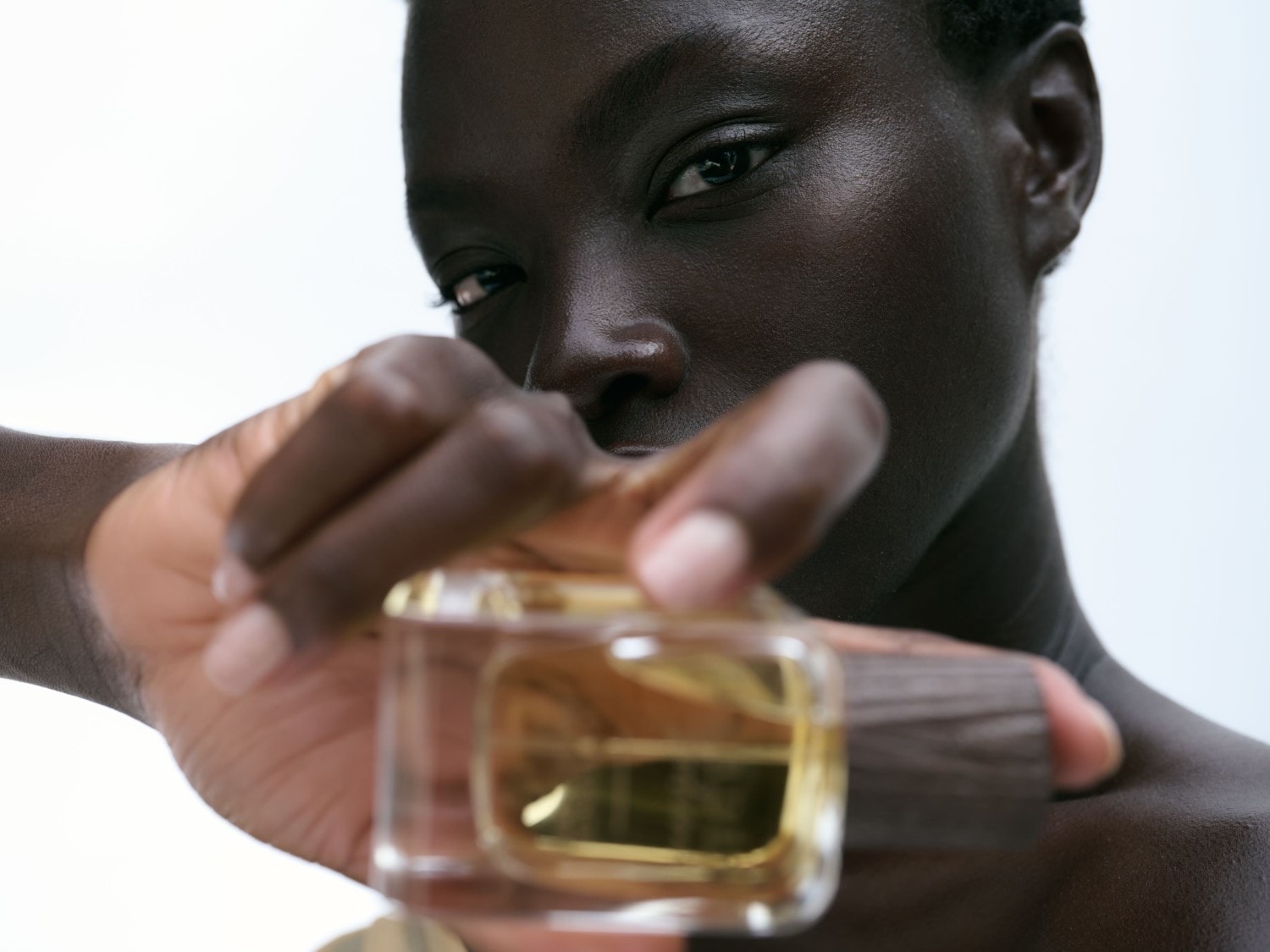 Kobieta trzyma w dłoni flakon perfum o przezroczystym szkle i drewnianym korku, prezentując jego elegancki design.