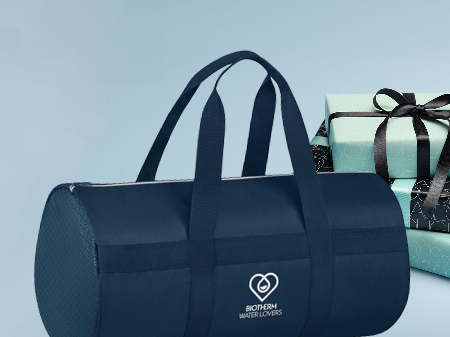 Granatowa torba sportowa Biotherm Water Lovers z uchwytami i logo obok stosu prezentów w ozdobnych papierach i czarnych wstążkach.