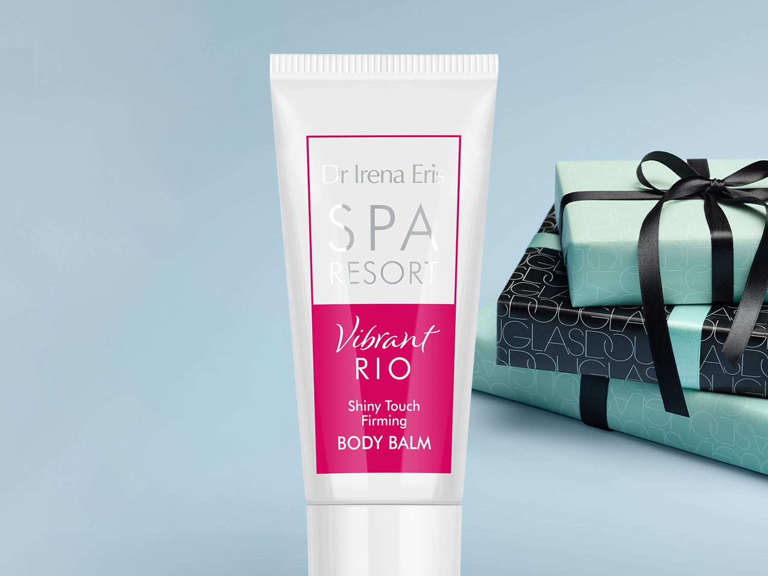 Biała tuba balsamu do ciała Dr Irena Eris SPA Resort Vibrant Rio Shiny Touch Firming Body Balm na tle prezentów.