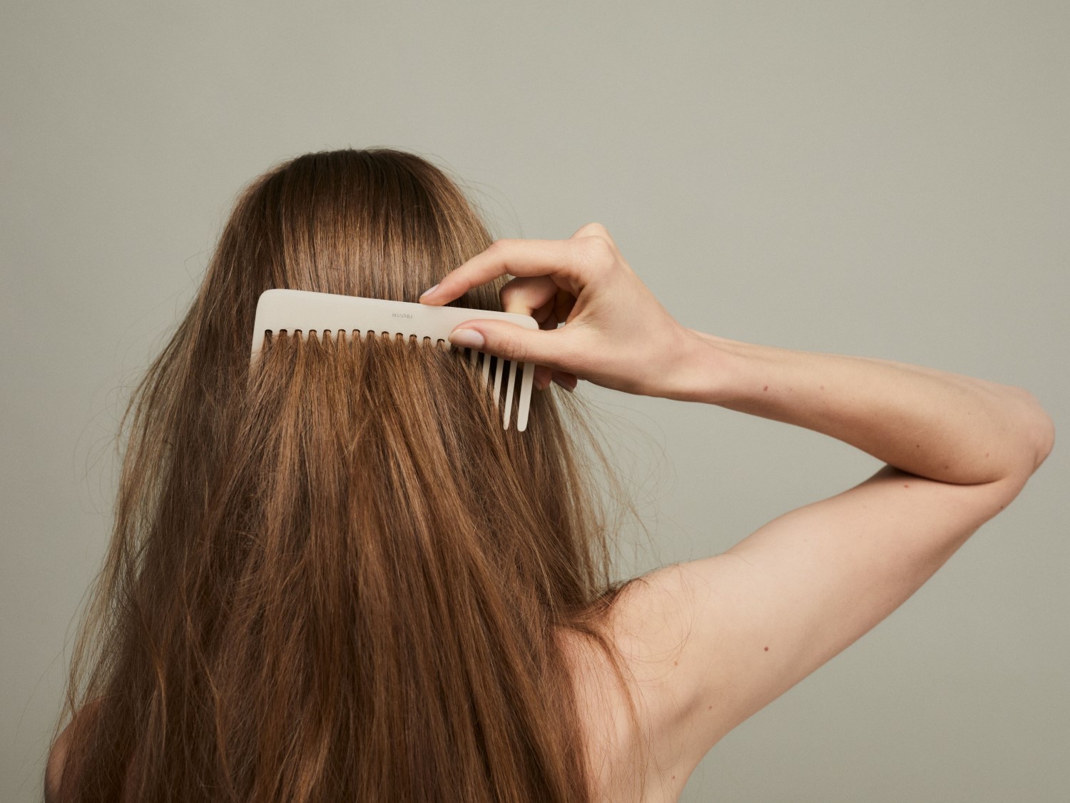 Eine Frau kämmt ihr langes, braunes Haar mit einem hellen Kamm, um es zu entwirren und zu glätten.