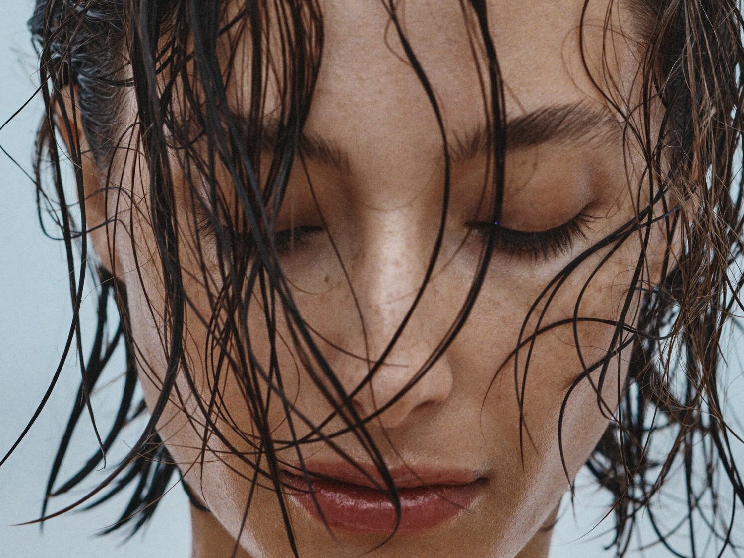 Nahaufnahme eines Frauengesichts mit geschlossenen Augen und nassen, dunklen Haaren, die ihr Gesicht umrahmen.