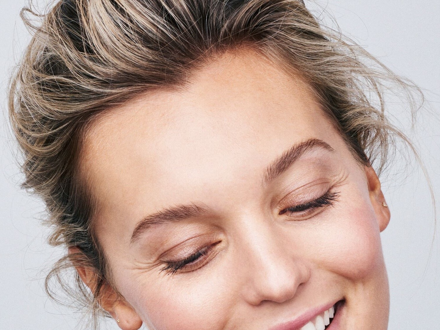 Nahaufnahme eines lächelnden Gesichts mit blonden Haaren, geschlossenen Augen und zarter Haut.