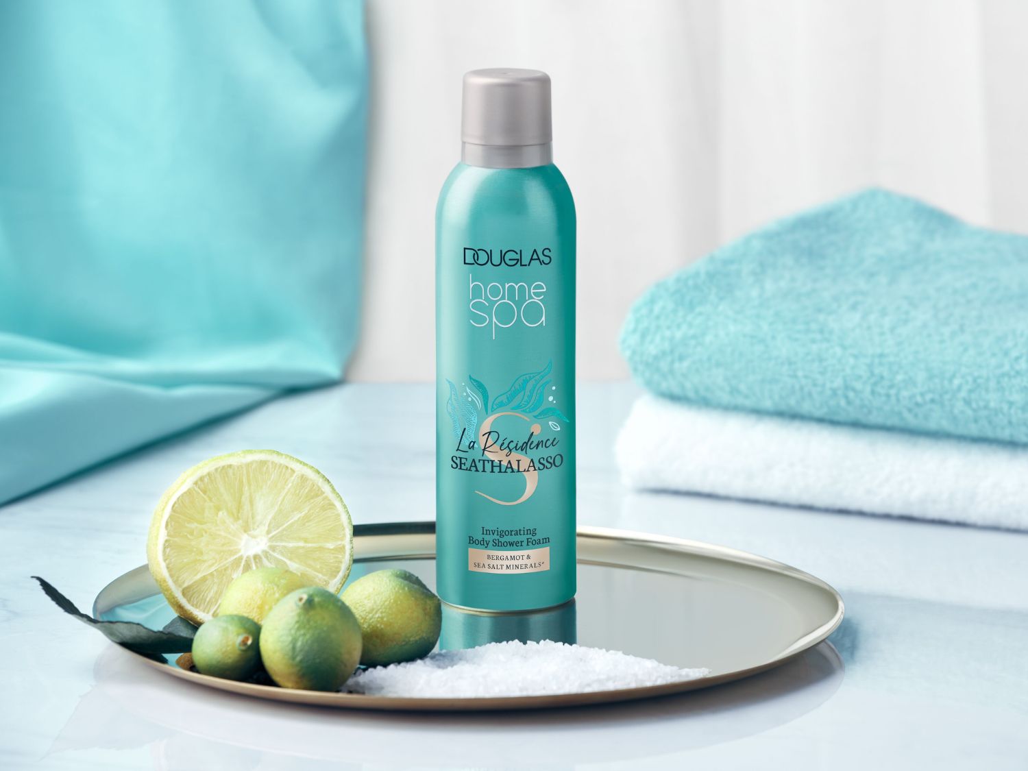 A Douglas Home Spa La Résidence Seathalasso frissítő tusolóhabja bergamottal és tengeri só ásványokkal, türkizkék flakonban, ezüst kupakkal, lime szeletekkel és tengeri sóval egy ezüst tálcán.