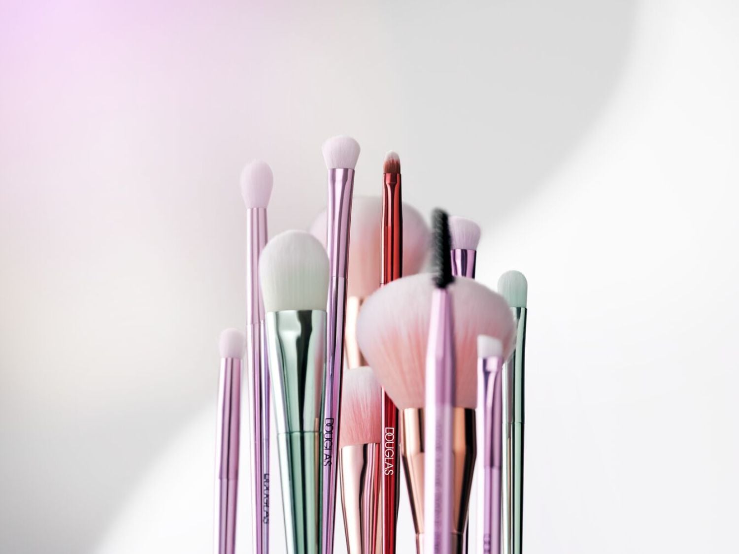 Különböző méretű és színű Douglas sminkecsetek láthatók, rózsaszín, ezüst és réz árnyalatokban, amelyek tökéletesek a teljes smink elkészítéséhez.