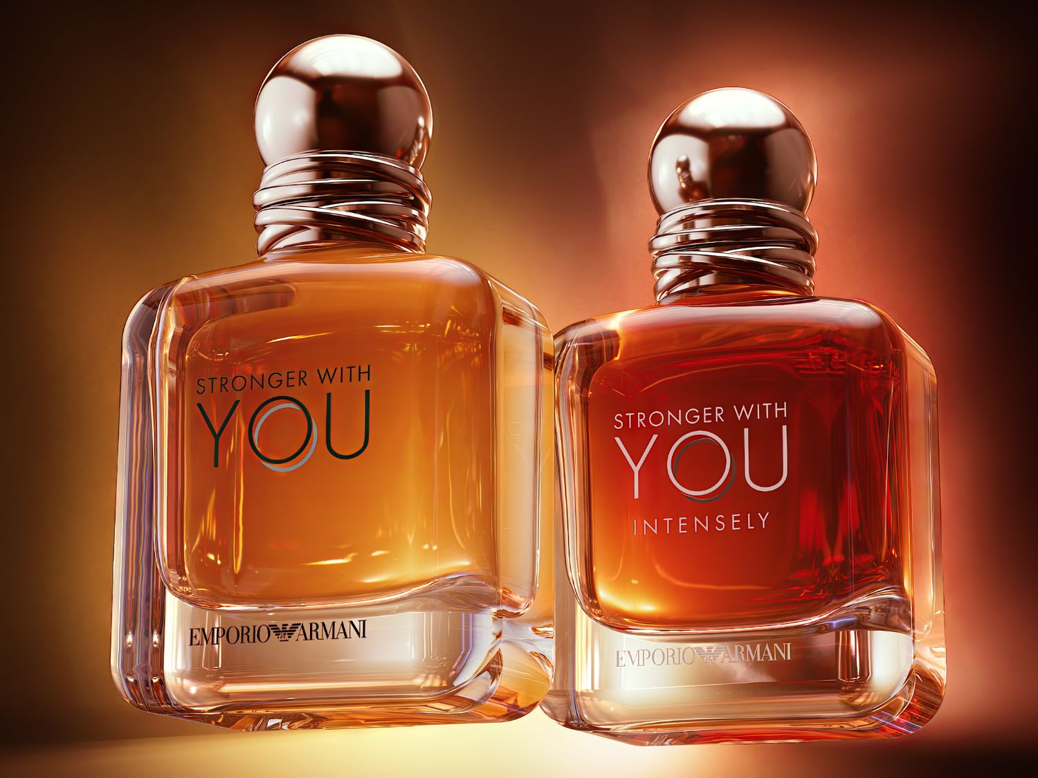 Két üveg Emporio Armani „Stronger With You” kölni látható, az egyik borostyánszínű, a másik mélyvörös, mindkettőnek fényes, bronz színű kupakja van, és az „Emporio Armani” felirat szerepel az üvegen.