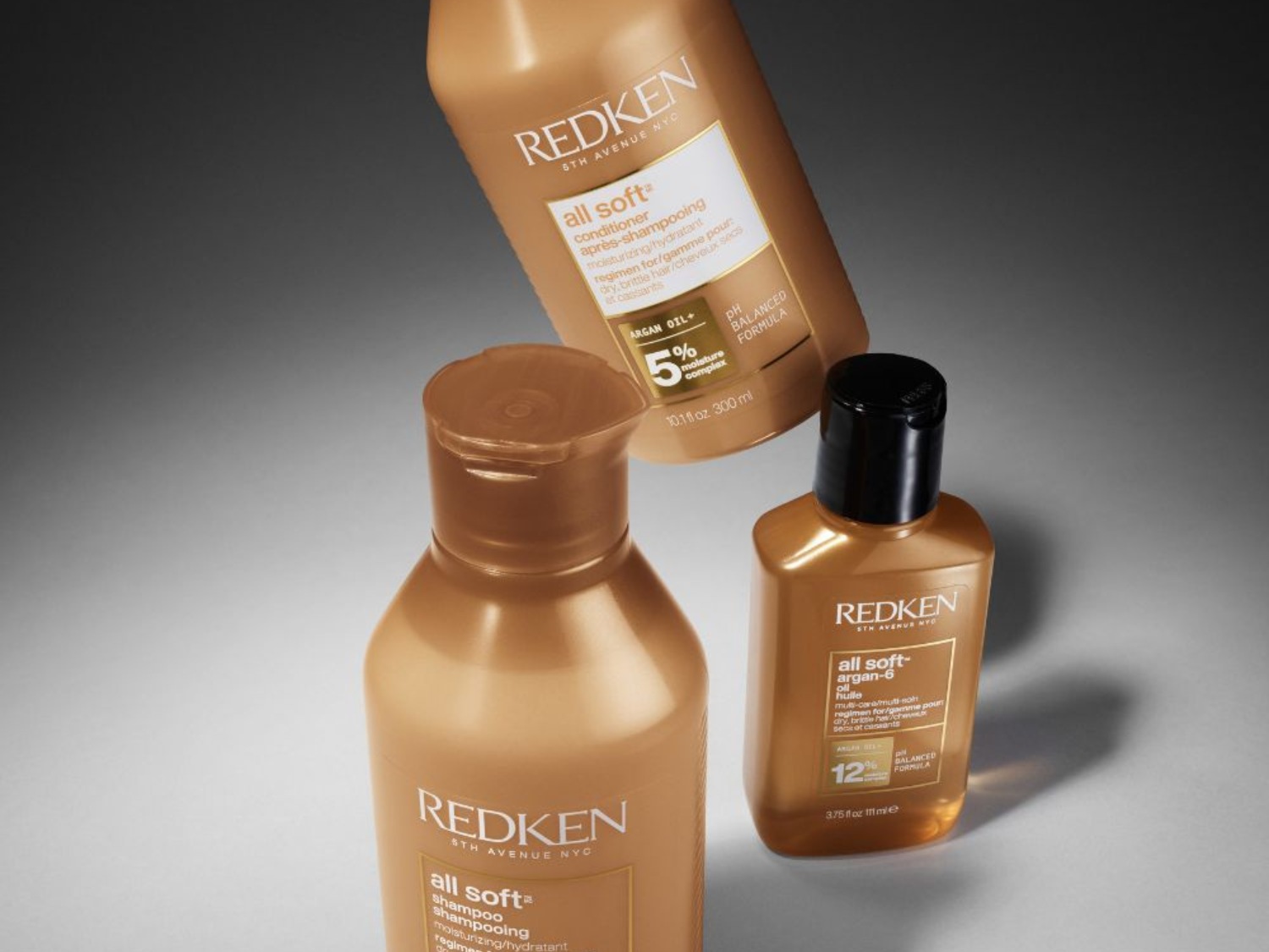 Tři zlatavé lahve Redken All Soft: kondicionér s 5% hydratačním komplexem, šampon a arganový olej s 12% oleje pro suché a lámavé vlasy.