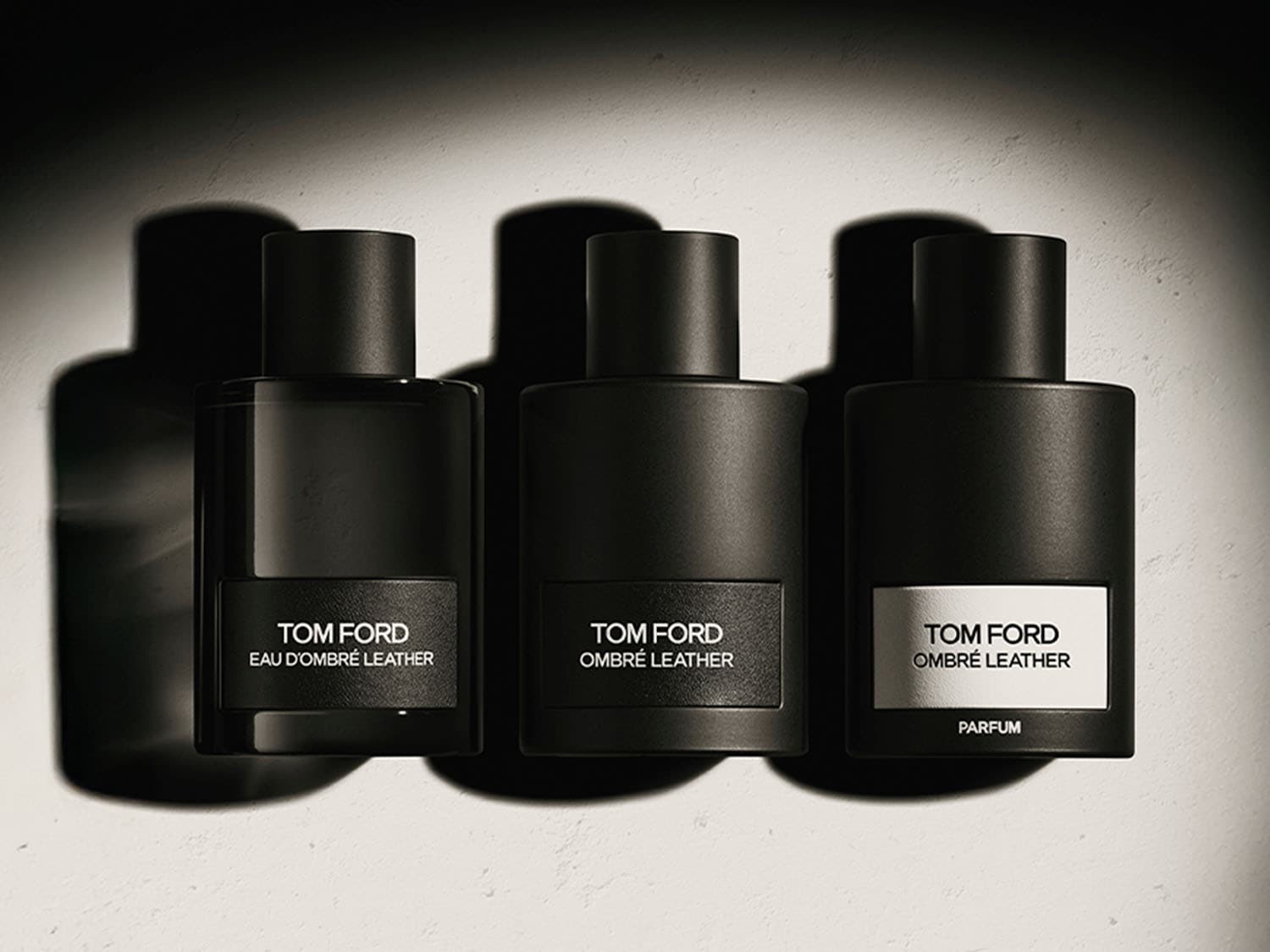 Tres frascos negros de perfume Tom Ford Ombre Leather, cada uno con una etiqueta diferente: Eau D'Ombre Leather, Ombre Leather y Ombre Leather Parfum.