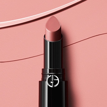 Detailný záber na rúž v čiernom obale s logom, odtieň je jemne ružový, na pozadí sú ťahy rúžu.