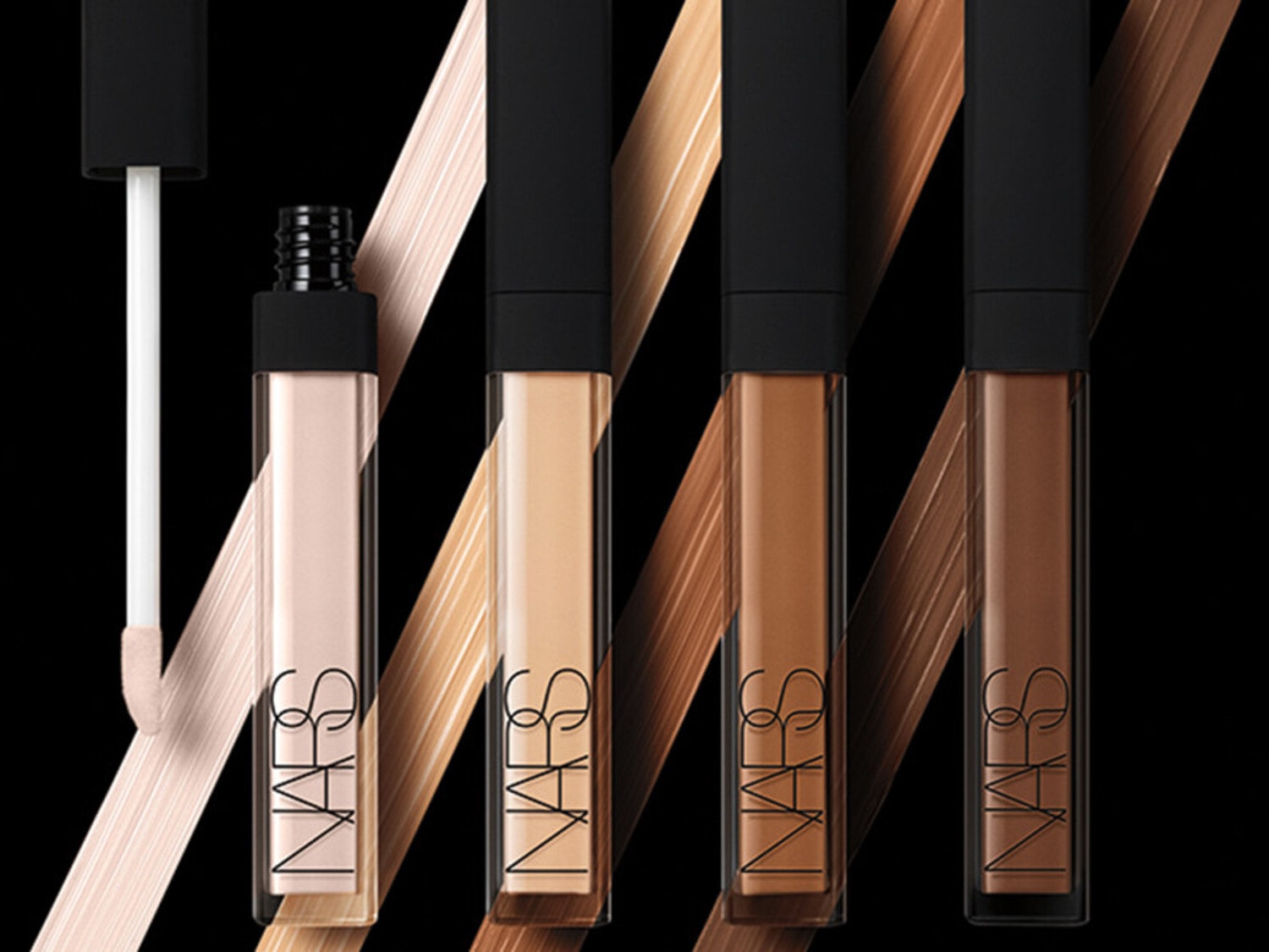 Quattro correttori NARS in diverse tonalità, dal beige chiaro al marrone scuro, con applicatore a spugnetta, su sfondo nero con pennellate di colore.