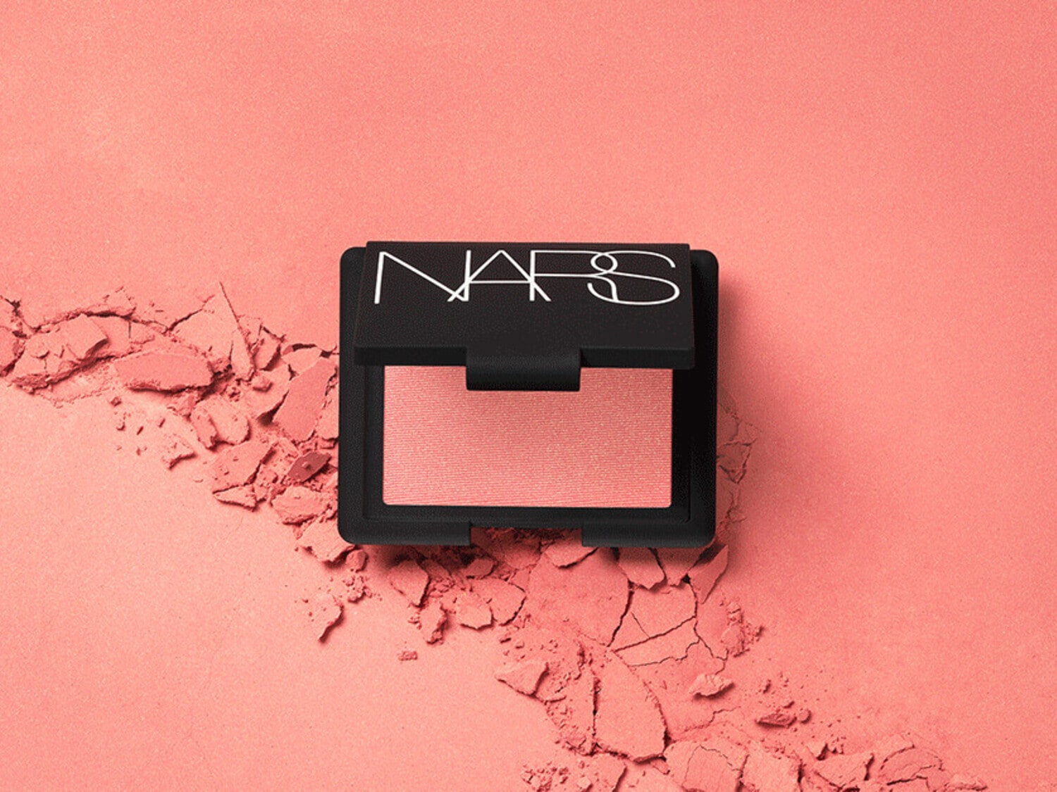 Fard in polvere compatto NARS color pesca chiaro, confezione nera con logo bianco, su sfondo pesca con polvere sparsa.