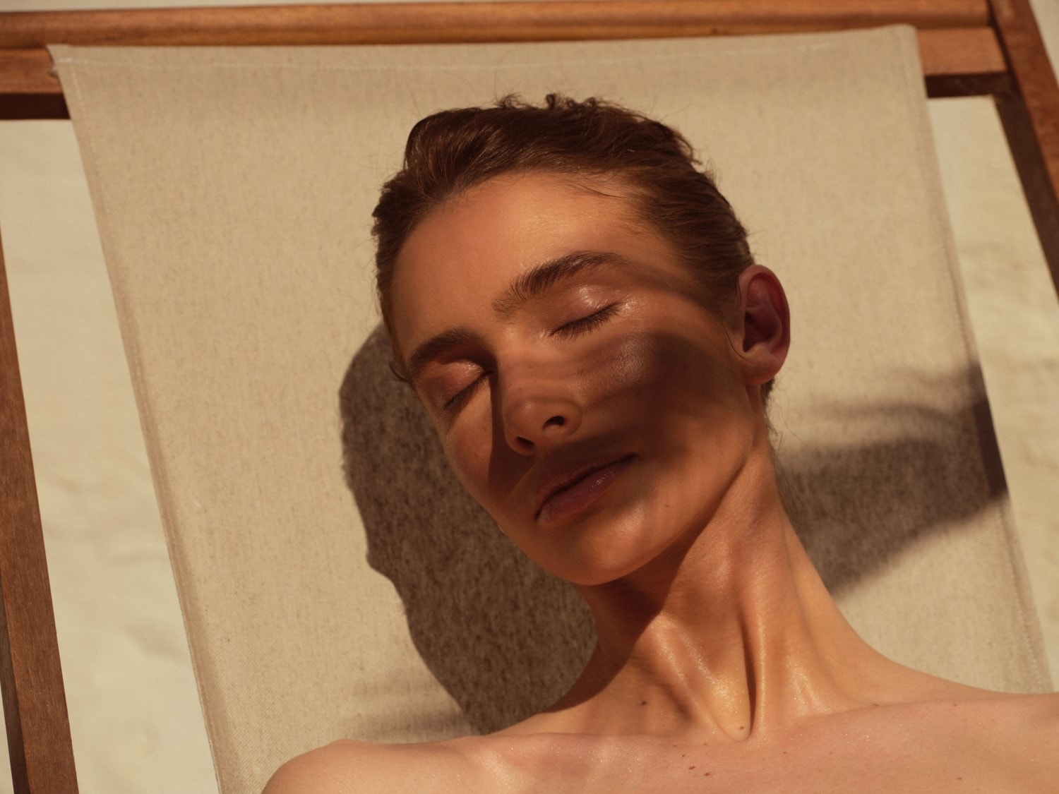 Eine Frau mit geschlossenen Augen liegt auf einem Liegestuhl, während Sonnenlicht ihr Gesicht und ihren Hals berührt.