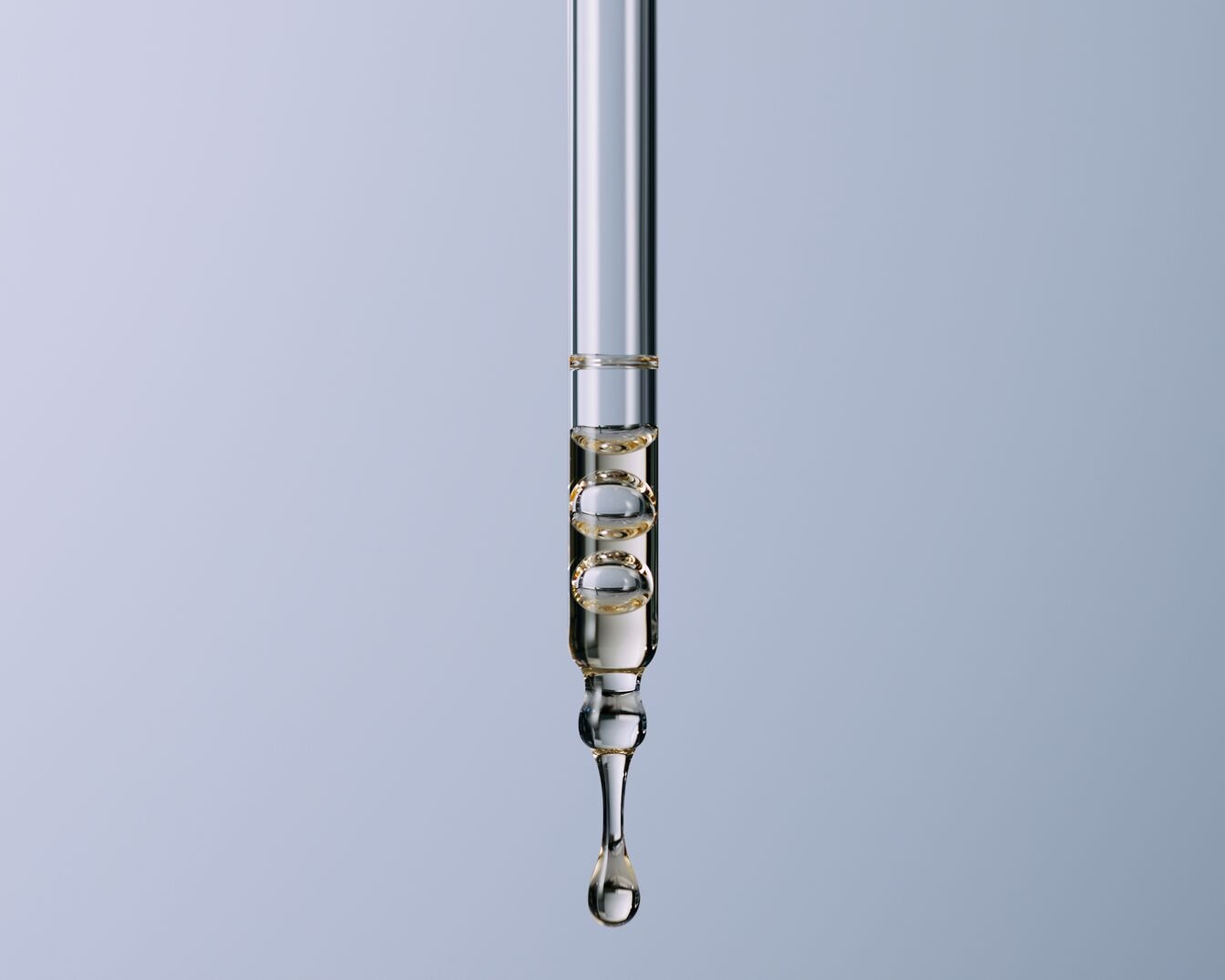 Nahaufnahme eines transparenten Glaspipette mit goldenem Serum und Luftblasen, das einen einzelnen Tropfen freisetzt.