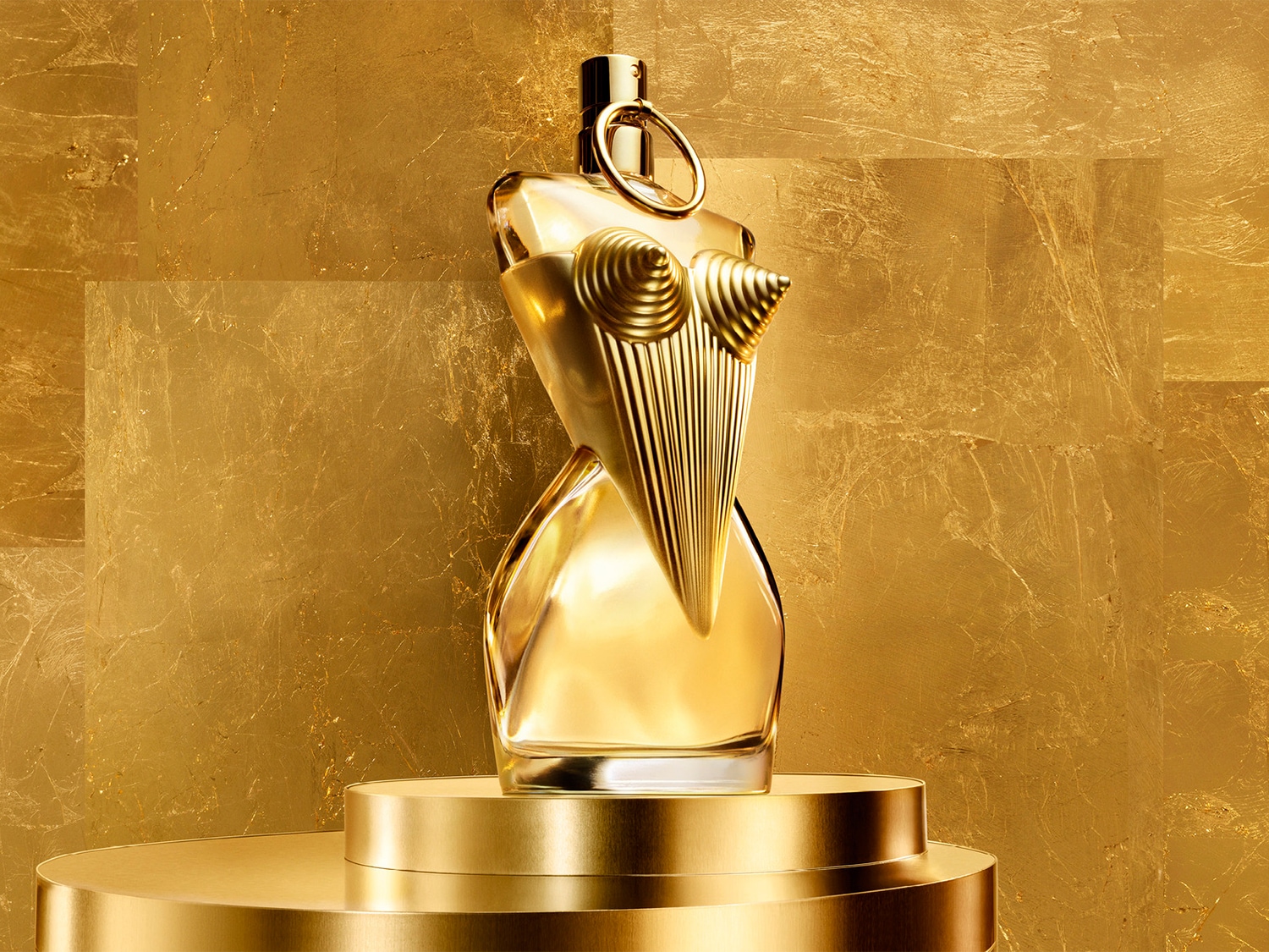 El frasco de perfume dorado con forma de torso femenino se alza sobre una plataforma dorada, irradiando lujo y sofisticación.