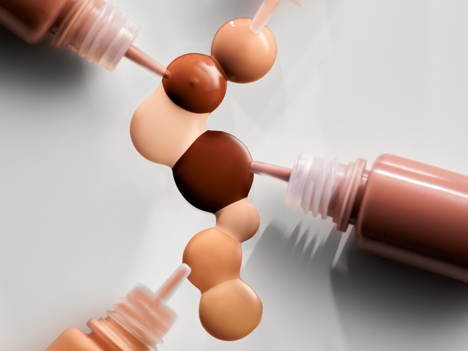 Verschillende tinten foundation, variërend van licht tot donkerbruin, worden uit flesjes met een roze-bruine dop gedoseerd.