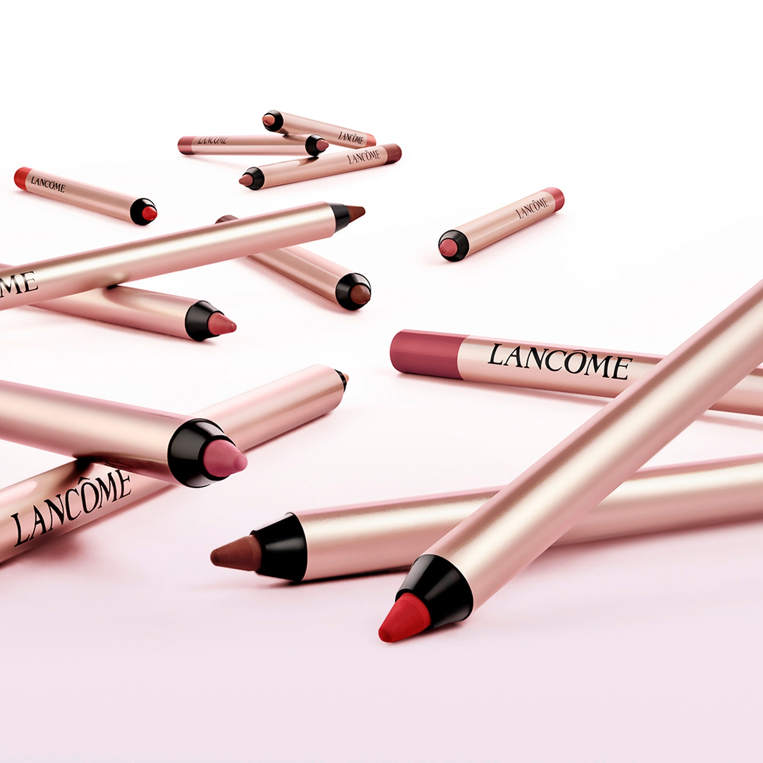 Nahaufnahme von Lancôme Lippenstiften in verschiedenen Farbtönen, die auf einer hellrosa Oberfläche verstreut sind und ein elegantes und anspruchsvolles Gefühl vermitteln.