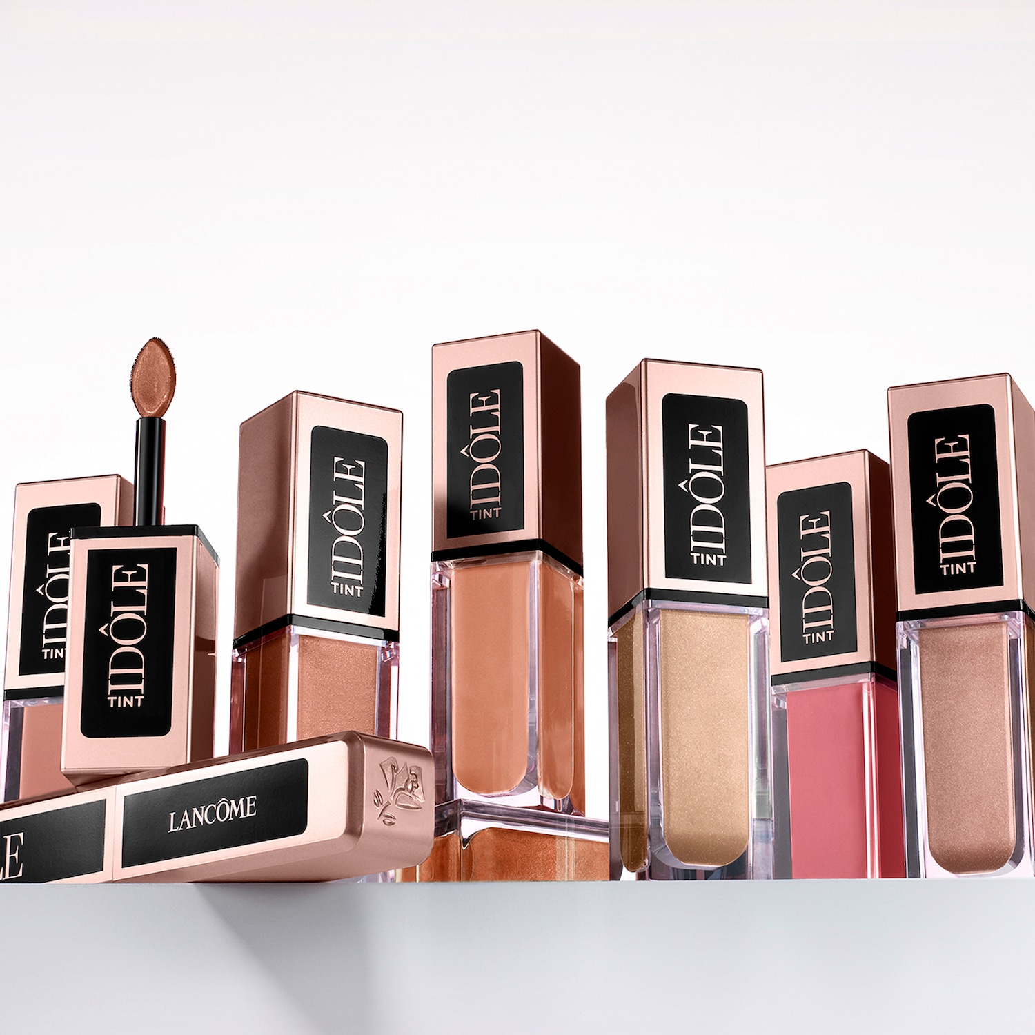Eine Kollektion von Lancôme Idôle Tint Lippenfarben in verschiedenen Nude- und Rosatönen, präsentiert in eleganten, quaderförmigen Flakons mit goldenen Akzenten.