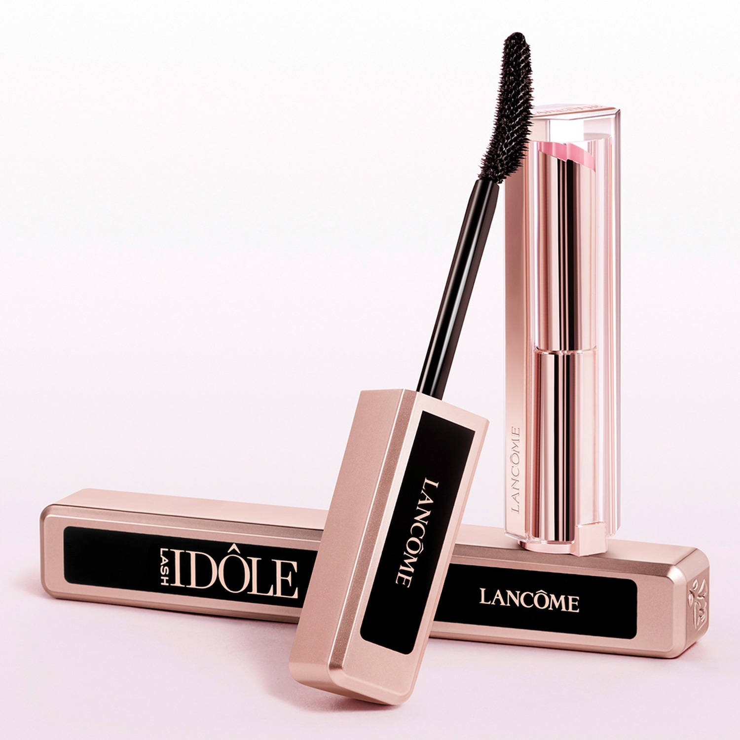 Nahaufnahme von Lancôme Lash Idôle Mascara in einer goldenen Verpackung mit schwarzer Schrift, daneben ein Lippenstift in einer transparenten Hülle.
