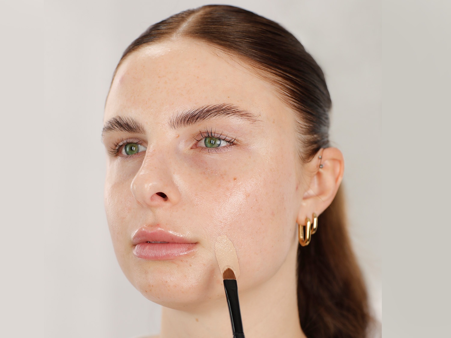 Nahaufnahme eines Gesichtes, auf das mit einem Pinsel helle Foundation aufgetragen wird, um einen ebenmäßigen Teint zu erzielen.