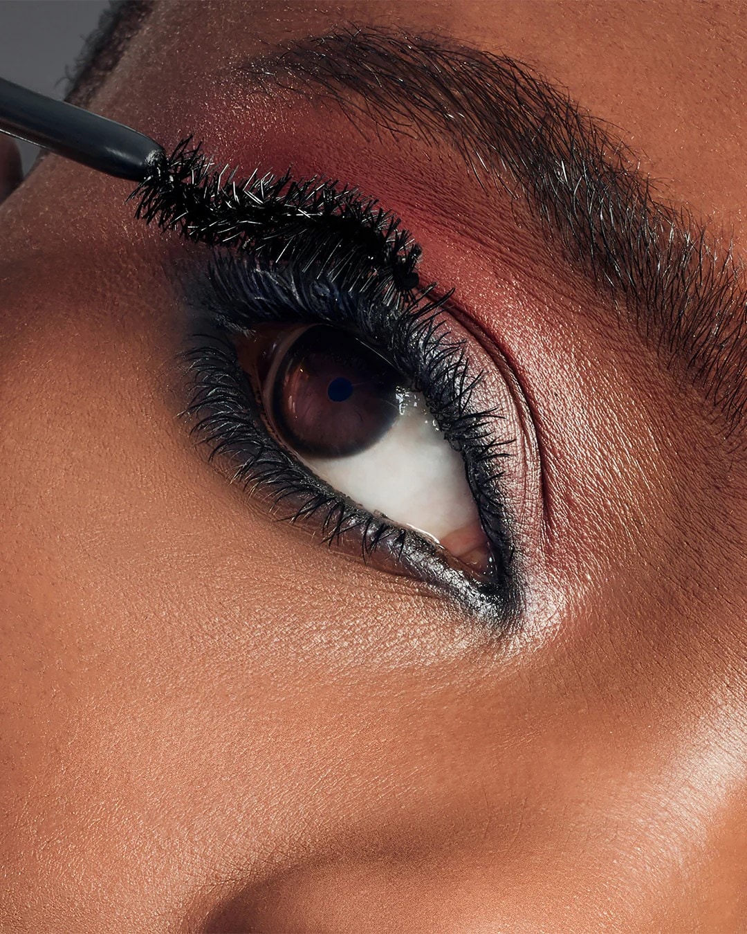 Nahaufnahme eines Auges mit dunkler Mascara, die auf die oberen Wimpern aufgetragen wird, um einen dramatischen Look zu erzielen.