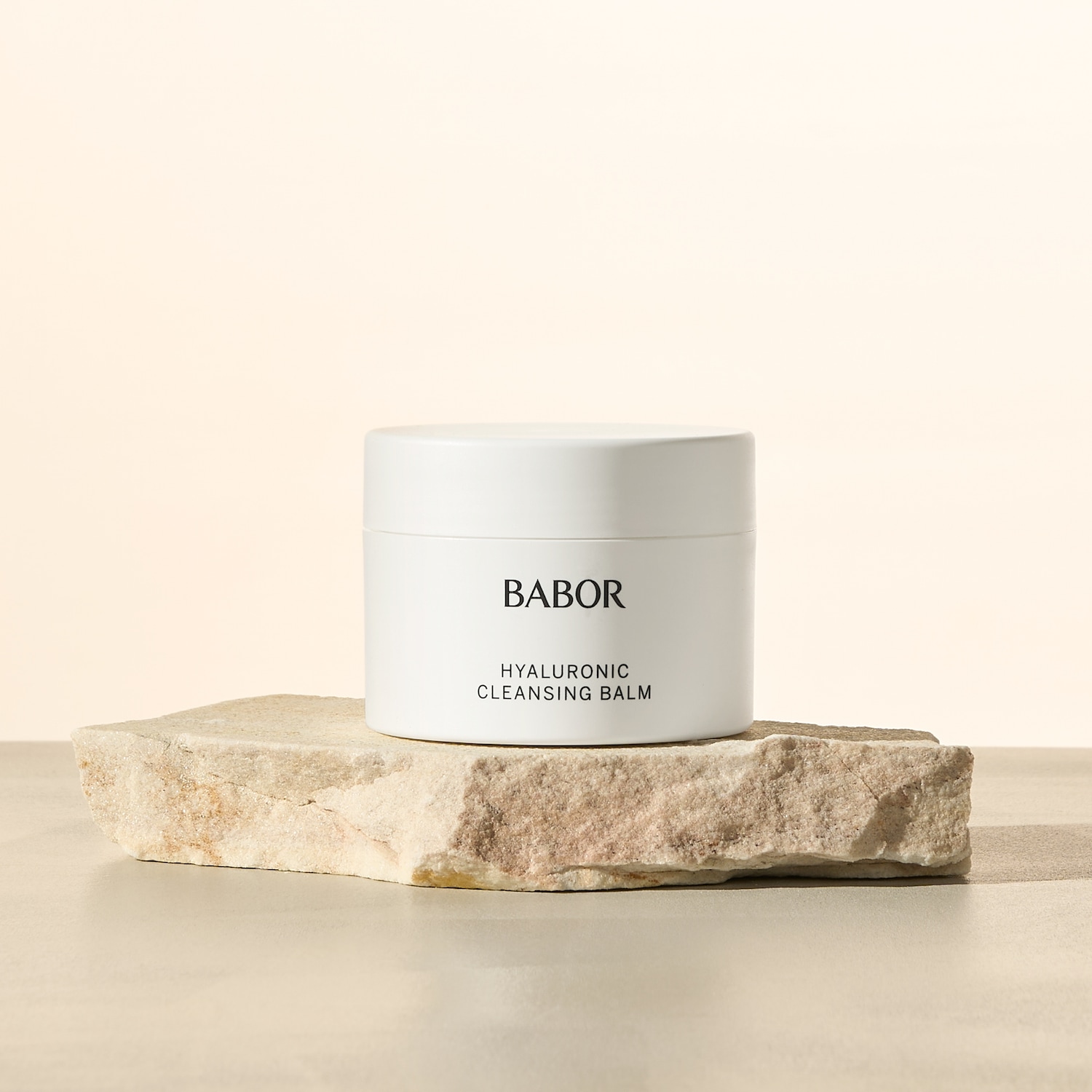 Biały słoiczek z napisem BABOR Hyaluronic Cleansing Balm stoi na kamiennej podstawie, prezentując produkt do oczyszczania twarzy.