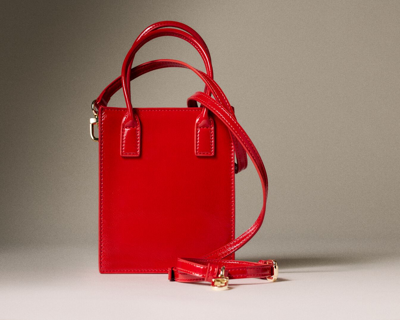 Quadratische, rote Lackledertasche mit Tragegriffen und abnehmbarem Schultergurt, die einen modernen und stilvollen Look verleiht.